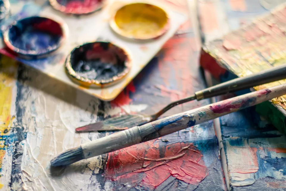 Paintbrushes and a palette on a paint-covered studio surface.
