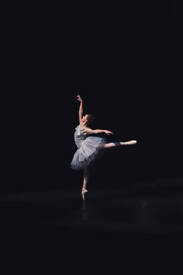 Ballet dancer performing a leap on a dark stage.