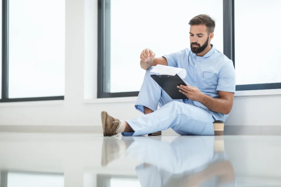 Healthcare professional in blue scrubs reviewing a clipboard.