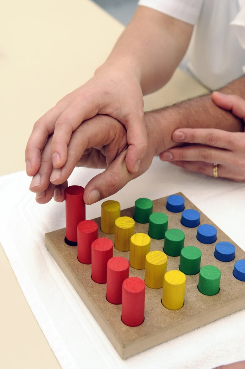 Therapist guiding a hand exercise with a colorful pegboard.