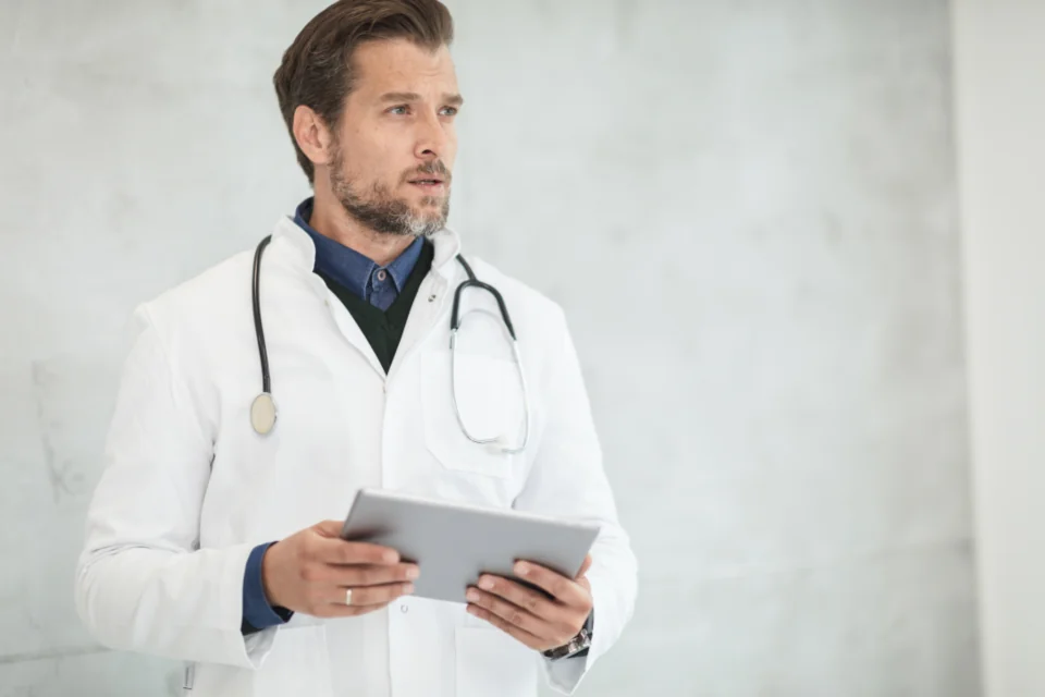 Healthcare professional wearing a white coat and holding a tablet.